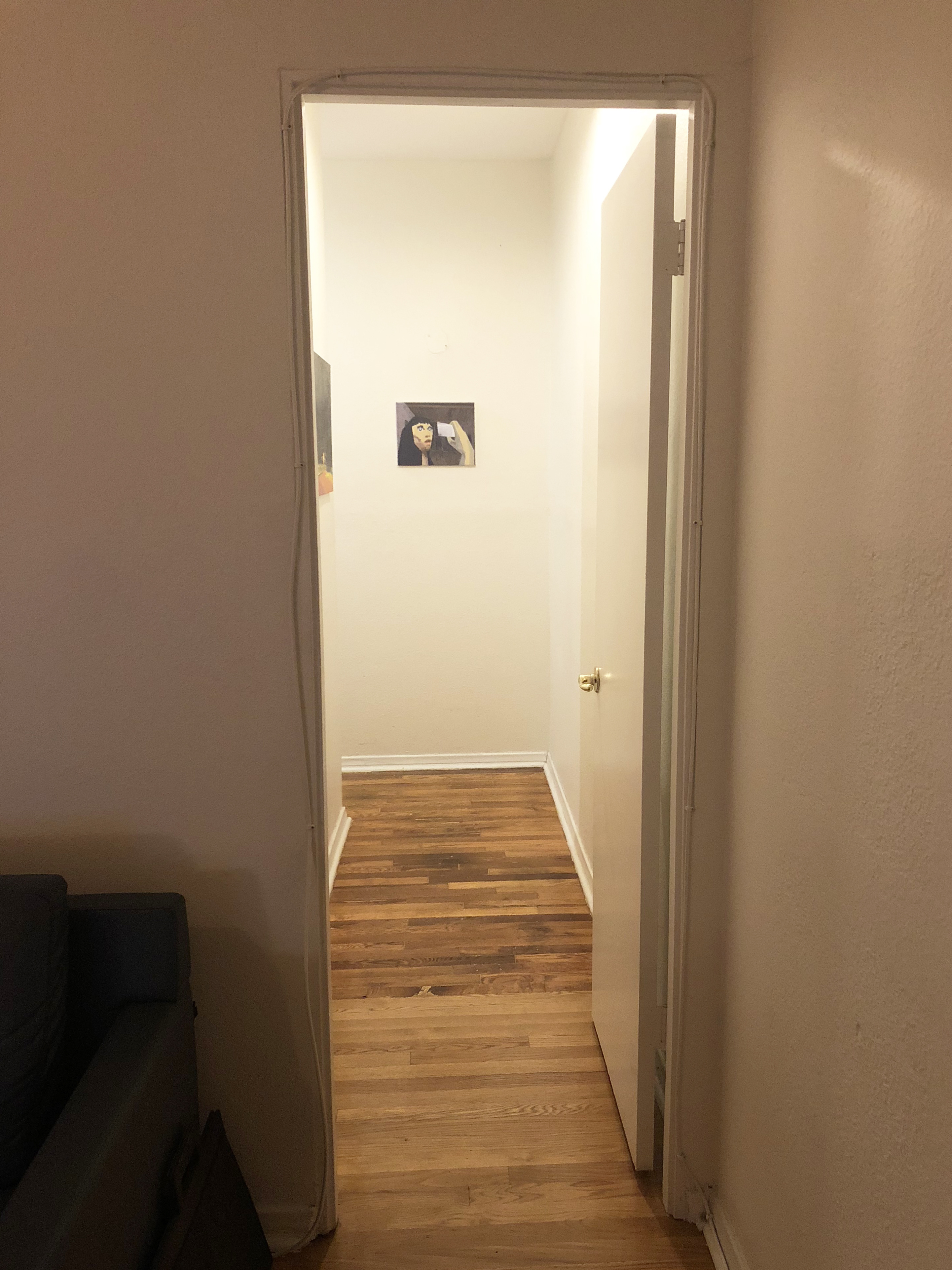 A narrow hallways with white walls seen through an open door